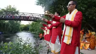 Priests offering dhoop incense by Canadian river with onlookers on footbridge